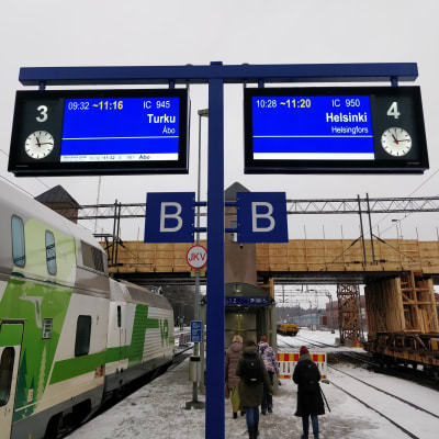 Informationstavlor visar att det är stora förseningar i tågtrafiken. Till vänster syns ett grönvitt Intercitytåg.