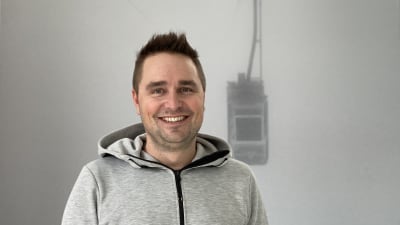 en man i grå tröja med en grå tavla bakom sig. På tavlan motiv av en skidhiss. 