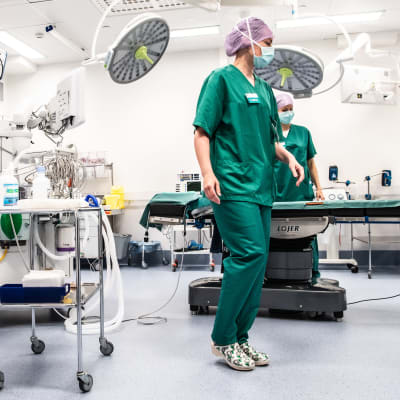 Sjukskötarna Carita Vuorenpää och Lotta Lantto arbetar i en operationssal på Jorvs sjukhus i Esbo, klädda i gröna sjukhuskläder och munskydd. 