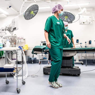 Sjukskötarna Carita Vuorenpää och Lotta Lantto arbetar i en operationssal på Jorvs sjukhus i Esbo, klädda i gröna sjukhuskläder och munskydd. 