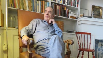Författaren Jörn Donner sitter framför sin bokhylla