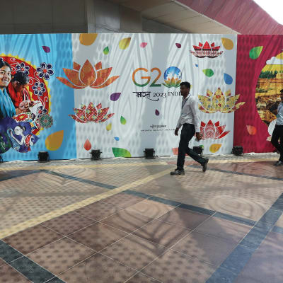 Kaksi henkilöä kävelee G20-kokousta markkinoivan julisteseinän edustalla.