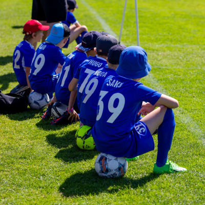 Sex unga fotbollsspelare sitter på rad på varsin fotboll.