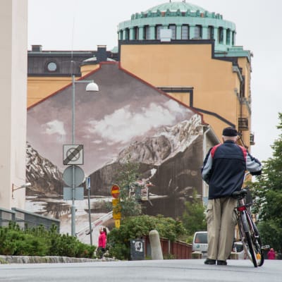 Gatuvy med en cyklist i förgrunden och en väggmålning i bakgrunden.