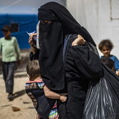 En kvinna bär på sitt barn och sina tillhörigheter i lägret al-Hol i nordöstra Syrien den 3 juni 2019. Kurdiska myndigheter började sända hem cirka 800 syriska kvinnor och barn som tidigare i år evakuerades från IS "kalifat".