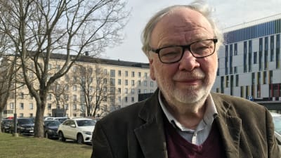 En man med glasögon och grått hår tittar in i kameran. Han står på en gräsmatta och bakom honom syns bilar och träd.