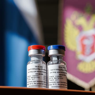 Kaksi rokotepulloa, taustalla Venäjän valtion vaakuna