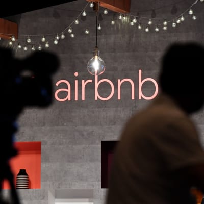 Aibnb:s logga på en vägg med skuggor av personer i fögrunden.