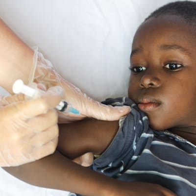 En liten pojke ligger på en säng och får vaccin i armen.