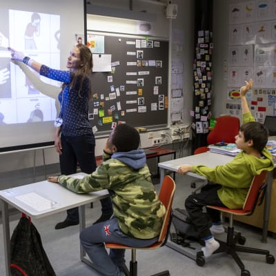 Erityisluokan opettaja Johanna Mäki opettaa oppilaille kuvien avulla suomenkielisiä sanoja. Oppilaina ovat Ramadan Dawuda ja Aleksei Zuev.