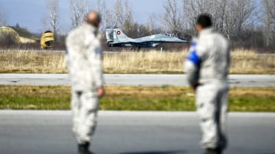 Ett jaktplan av typen MiG-29 landar. I förgrunden står två piloter.
