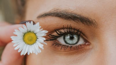 En närbild på en kvinnas halva ansikte och en liten blomma hon håller vid ögat.