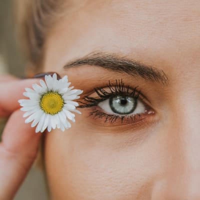 En närbild på en kvinnas halva ansikte och en liten blomma hon håller vid ögat.