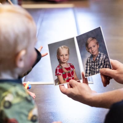 Taapero osoittaa koulukuvia, joissa kaksi vanhempaa lasta.
