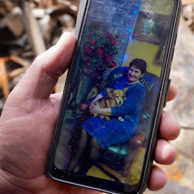 Miehen kädessä puhelin jossa kuva naisesta koira sylissä