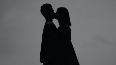 Två personer kysser varandra, svarta siluetter mot grå bakgrund