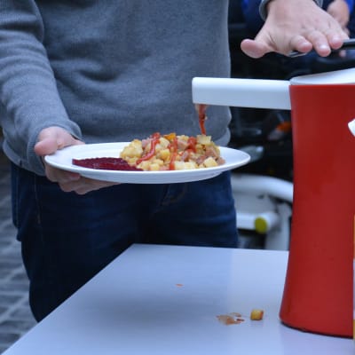 En person klämmer ketchup på sin pyttipanna i en skolmatsal.