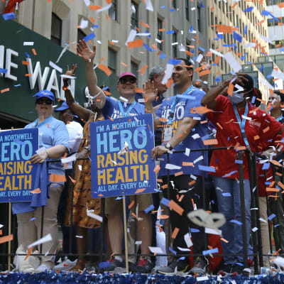 Ett gäng människor med skyltar som tackar för hälsovårdarnas arbete under coronapandemin. Runt människorna ses mängder med konfetti.