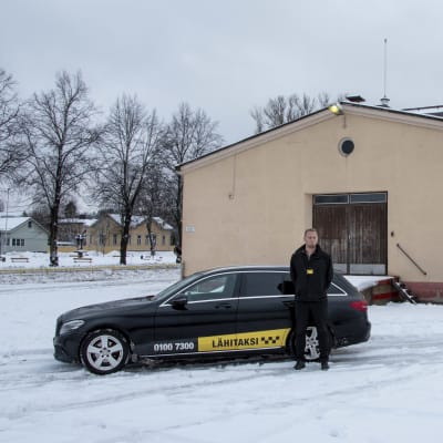 Taxichaufför Toni Ahlfors intill sin taxibil som han parkerat utanför Lovisa busstation.