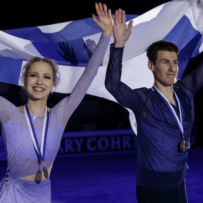 Juulia Turkkila och Matthias Versluis vinkar mot publiken med Finlands flagga.