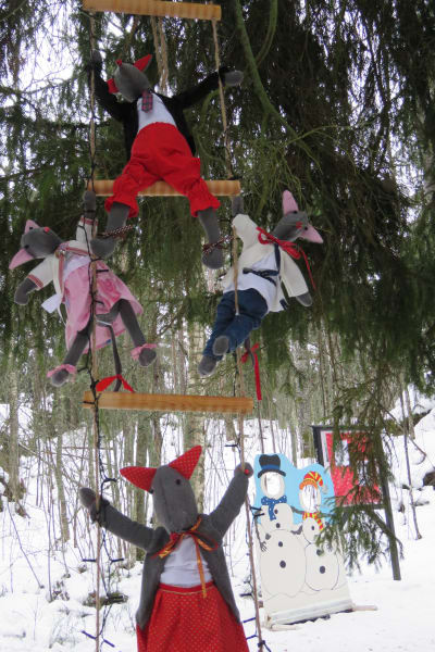 Röda, handgjorda jultomtar i tyg, eller kanske möss i människokläder, hänger i repstege ute i vinterlandskap. Julstigen i Hangö 2022.