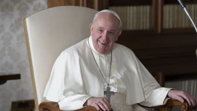 Påven Franciskus sitter på en stol och skrattar 
