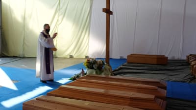 En präst välsignar en rad kistor i ett tält under coronaepidemin i norra Italien