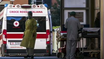 Ambulans och två personer i skyddsdräkt utanför ett italienskt sjukhus.