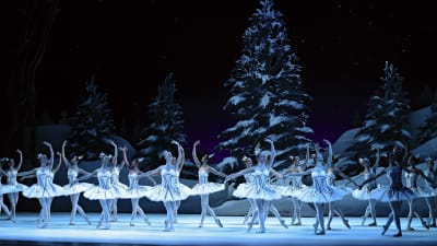 Lavan täydeltä balettitanssijoita valkoisissa asuissa tanssii kädet kohotettuna lumisen maiseman edessä.