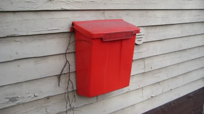 Röd postlåda på husvägg.