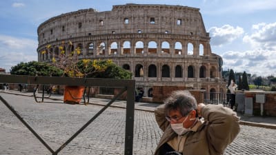 Man med munskydd framför Colosseum i Rom