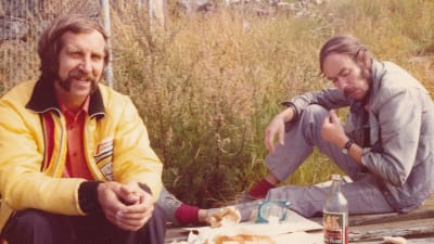 Arkivfoto från 1970-talet där två män äter medhavd matsäck ute i det fria.