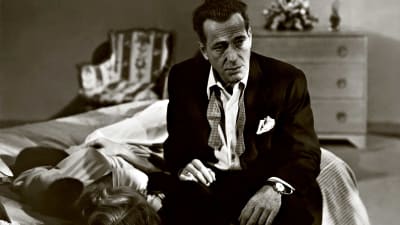 Huonovointisen näköinen mies (Humphrey Bogart) istuu paidan nappi ja solmuke auki sängyn laidalla. Kuva elokuvasta Hermot pinnalla (In a Lonely Place).