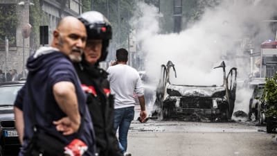 Nerbrunnen bil på en gatan i Milano i bakgrunden, några människor i förgrunden.