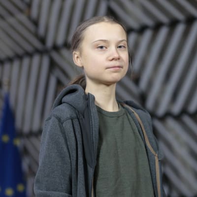 Greta Thunberg står framför Europeiska Unionens flaggor. 