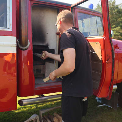 Antti Nisula laittaa puita saunan pesään, joka on tehty vanhaan paloautoon.