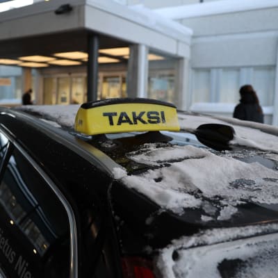 Taksi parkkeerattuna Lapin keskussairaalan edustalle, taustalla tuntemattomia henkilöitä.