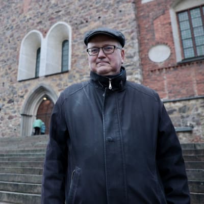Hannu Salmi mustassa takissa Turun Tuomikirkon portailla.