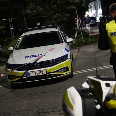 Tanskalainen moottoripyöräpoliisi selkä kameraan päin, ja poliisiauto kadulla iltapimeällä.