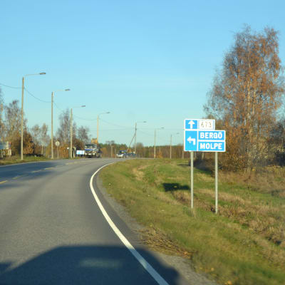 Två bilar kör på Strandvägen i Korsnäs. Blå skylt som visar pil till vänster mot Bergö och Molpe.
