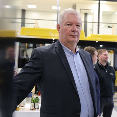 Energon myyntipäällikkö Mikko Summala katsoo kohti kameraa, taustalla Energon logo-takki päällä olevia työntekijöitä ja keltainen Föli-bussi.