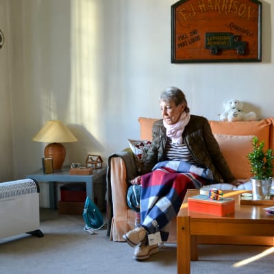 Sophie Foubert istuu sohvalla viltin alla, tikkitakki yllään. Sohvan vieressä on kannettava lämpöpatteri.