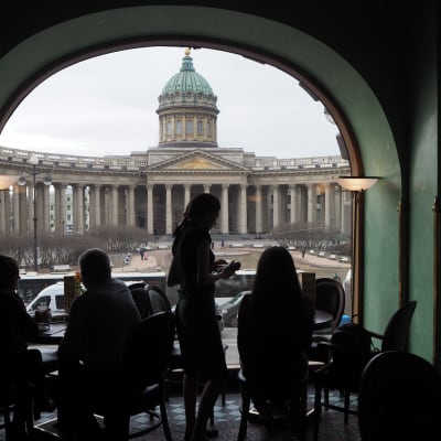 Vy från ett café i S:t Petersburg. I förgrunden syns människor som står framför ett bågformat fönster i motljus.