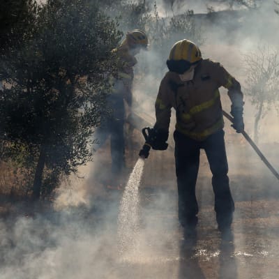 Två brandmän släcker markbränder i Katalonien. 