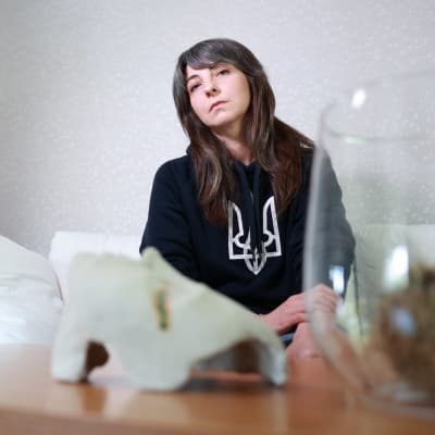 En mörkhårig kvinna sitter i en vit soffa i ett ljust vardagsrum.  I förgrunden syns ett kaffebord.