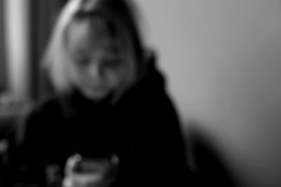 Någon anonym tittar ner på sin telefon. Bilder är svartvit och blurrad.