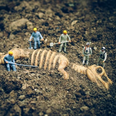 Pienet muovihahmot kaivavat dinosauruksen luurankoa esiin hiekasta.