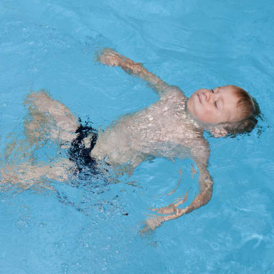 En pojke simmar ryggsim i en pool. 