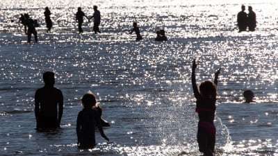 Ungdomar som simmar och vada i vatten. Det är i Helsingfors, Sandudds badstrand.