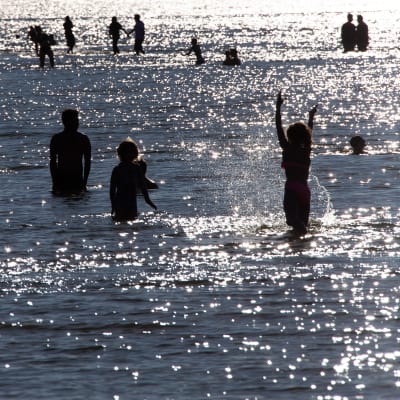Ungdomar som simmar och vada i vatten. Det är i Helsingfors, Sandudds badstrand.
